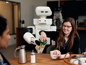 Eine Frau und ein Roboter schütten gemeinsam ein Getränk in eine Tasse.