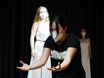 Drei junge Frauen mit Maske auf einer Bühne